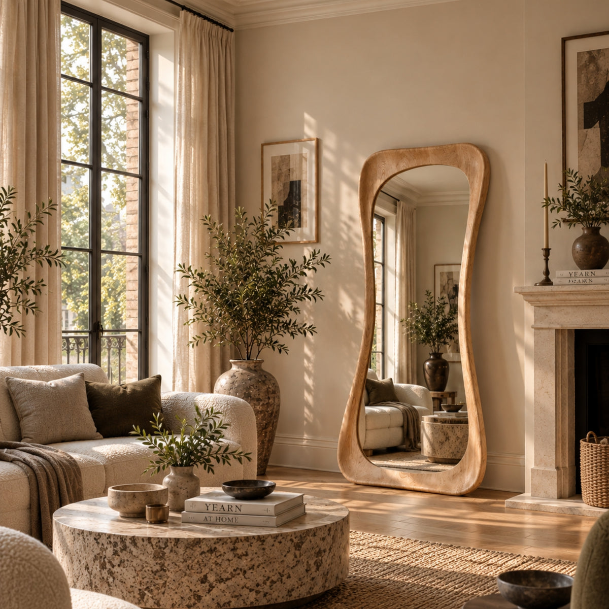 A large, full-length floor mirror with a wavy, organic wooden frame stands in a beautifully styled living room with warm sunlight streaming through windows.