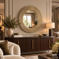 a round wall mirror with a textured gold frame hangs above a dark wood console table in a styled living room setting.