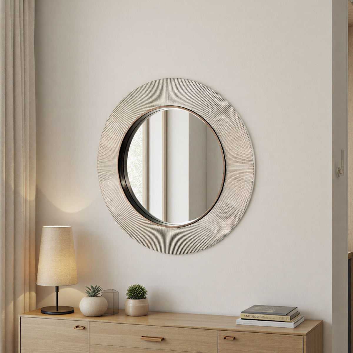 Round decorative mirror on a wall above a wooden console table with a lamp and plants.
