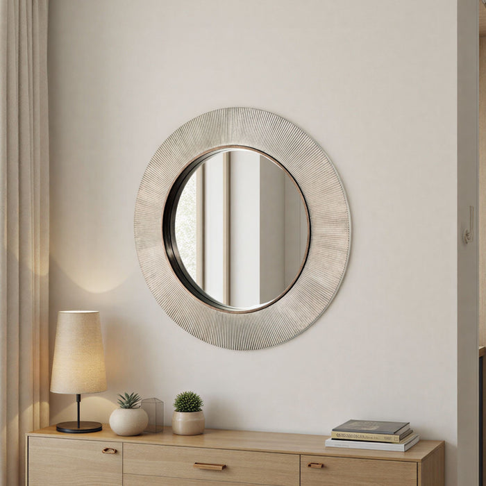 Round decorative mirror on a wall above a wooden console table with a lamp and plants.