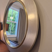 Round metallic mirror on a wall with a window reflection