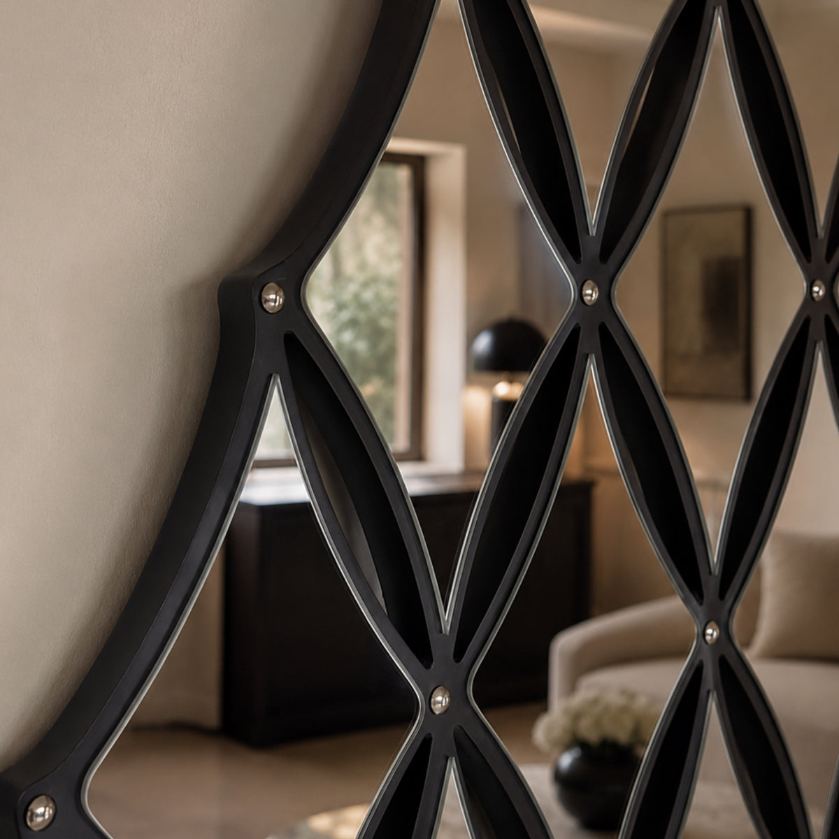 A close-up of a modern black metal screen or decorative wall divider with an interlocking geometric lattice pattern and small metallic rivets, set in a softly lit interior room.