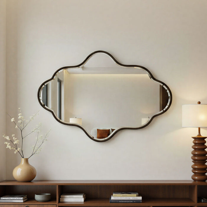Decorative wall mirror with a bronze frame on a neutral wall above a wooden shelf.
