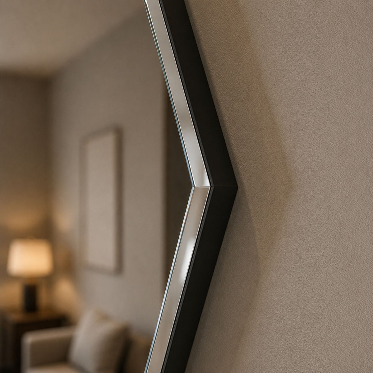A close-up of a modern geometric wall mirror with a black frame and silver reflective edge, mounted on a textured beige wall in a softly blurred living room setting.