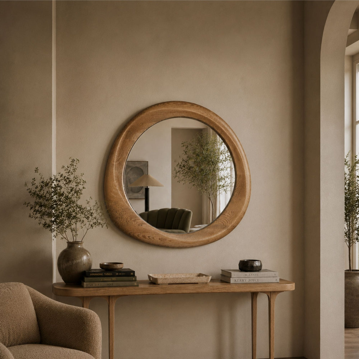 Round wooden wall mirror with a natural oak frame, hanging on a beige plaster wall above a wooden console table in a styled interior room.