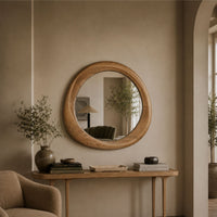 Round wooden wall mirror with a natural oak frame, hanging on a beige plaster wall above a wooden console table in a styled interior room.