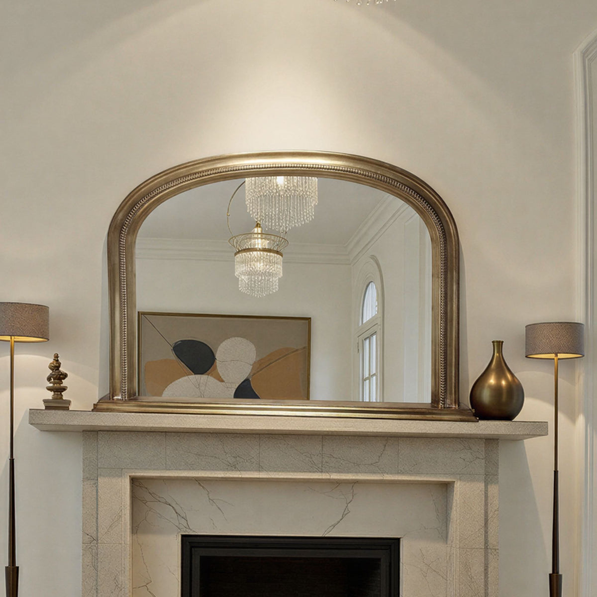 Decorative antique gold mirror above a fireplace with lamps on either side.