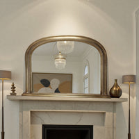 Decorative antique gold mirror above a fireplace with lamps on either side.