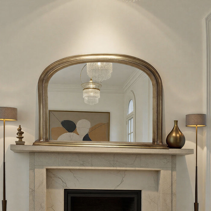 Decorative antique gold mirror above a fireplace with lamps on either side.