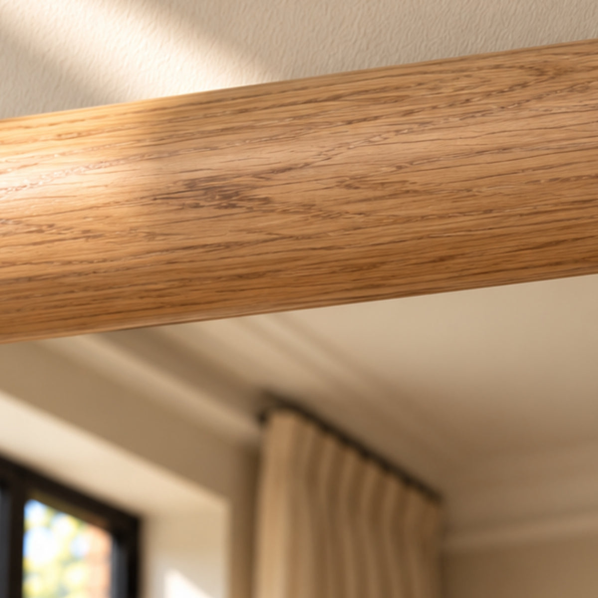 A close-up of a light oak wood grain trim or molding bar running diagonally across the frame, with a softly blurred interior room background showing a window and curtain.