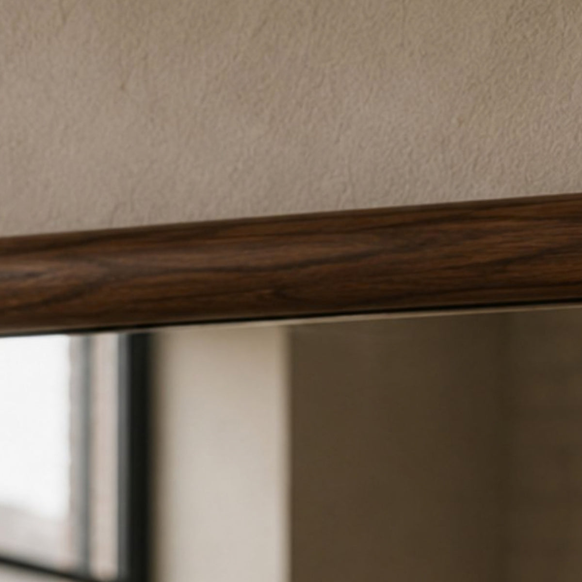 Close-up of a dark brown wood grain trim or shelf edge against a textured beige wall, with a blurred interior reflection below.