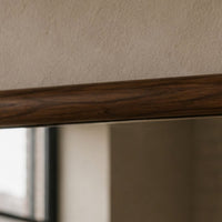 Close-up of a dark brown wood grain trim or shelf edge against a textured beige wall, with a blurred interior reflection below.