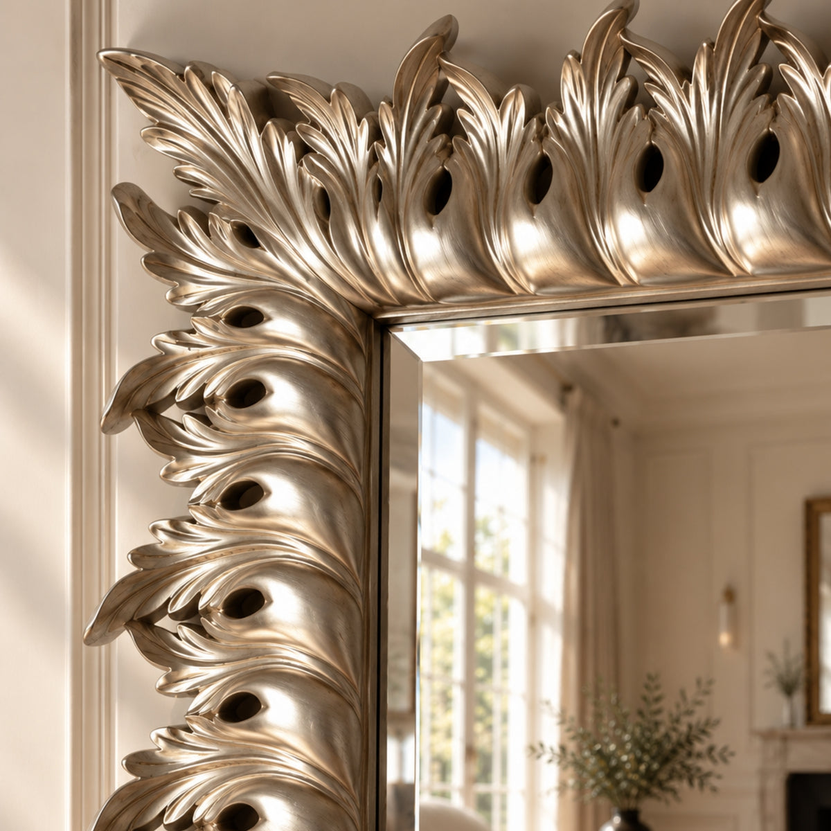 An ornate silver mirror frame with a highly detailed, sculpted acanthus leaf design, shown in a warm, elegant room setting.