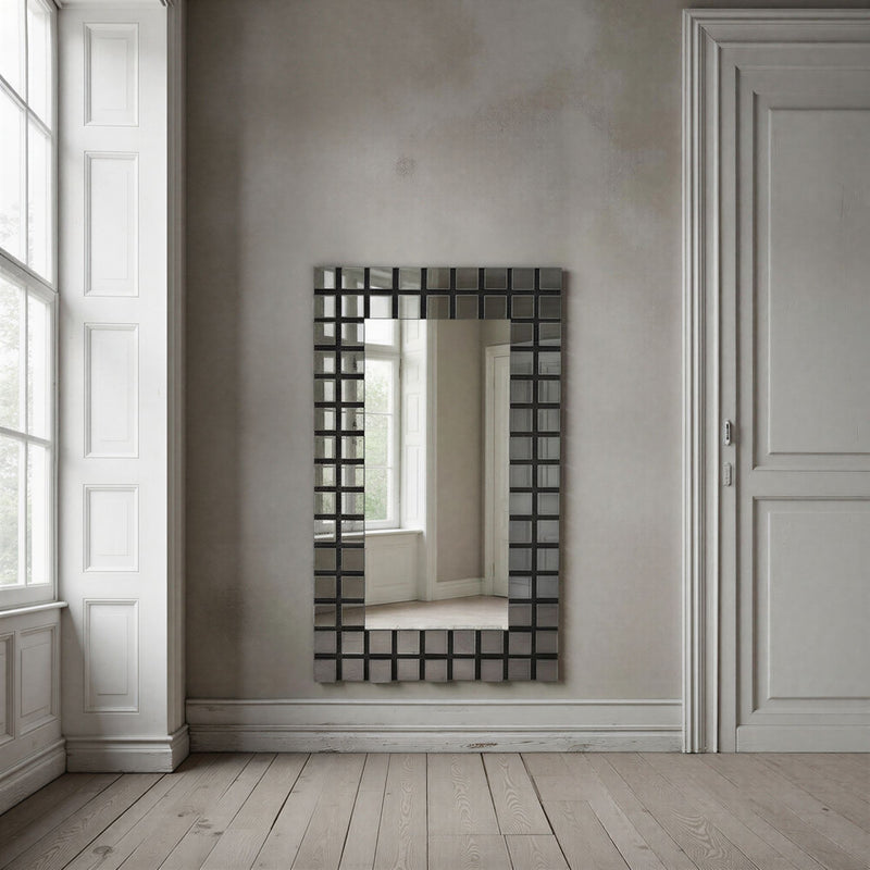 A rectangular wall mirror with a dark, geometric grid frame hangs on a textured gray wall in a bright, modern room with white paneled doors and light wood floors.