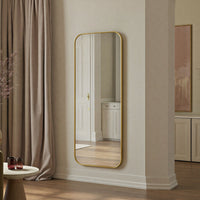 Full-length mirror with gold frame on a wall in a room with curtains and a side table.